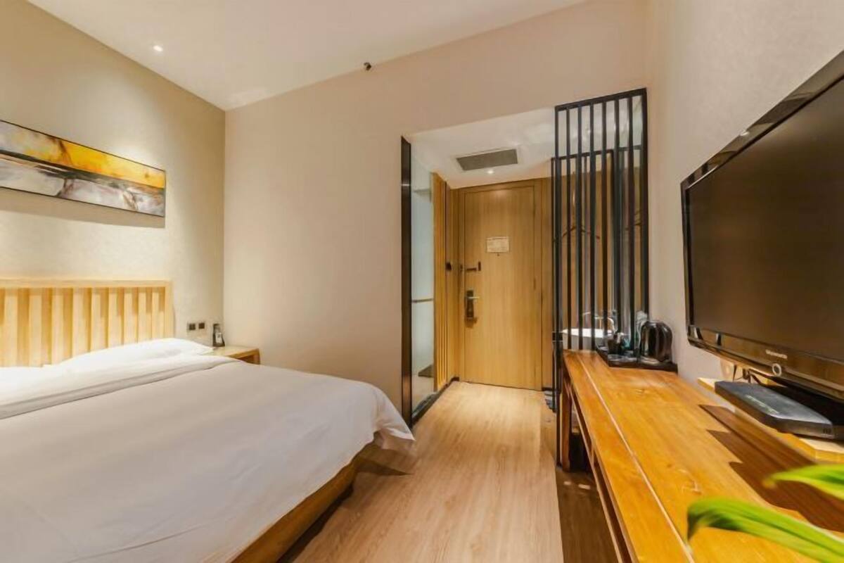 Une chambre d’hôtel avec un lit, un bureau en bois avec une télévision et un tableau au mur.