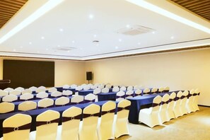 A conference room with rows of tables and chairs, a projector screen, and a speaker.