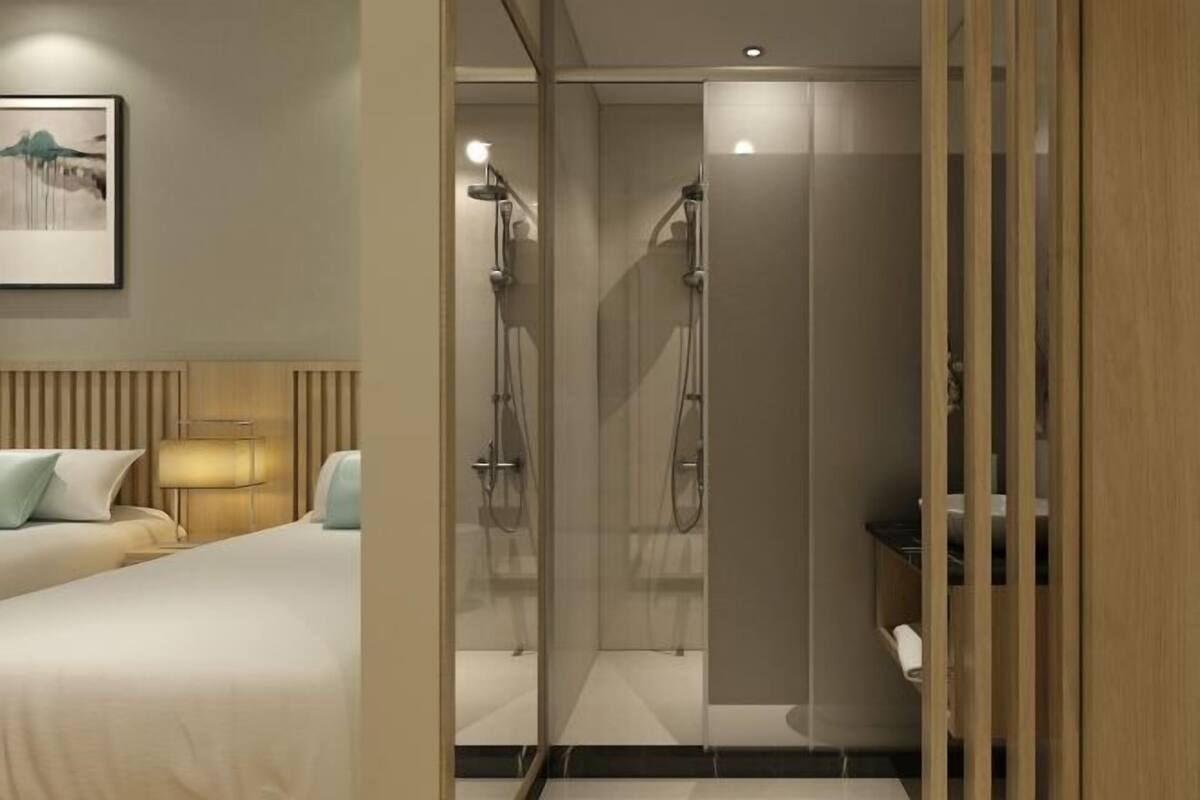 Une chambre d’hôtel moderne équipée d’un lit, d’une lampe de chevet et d’un espace douche avec des portes en verre.