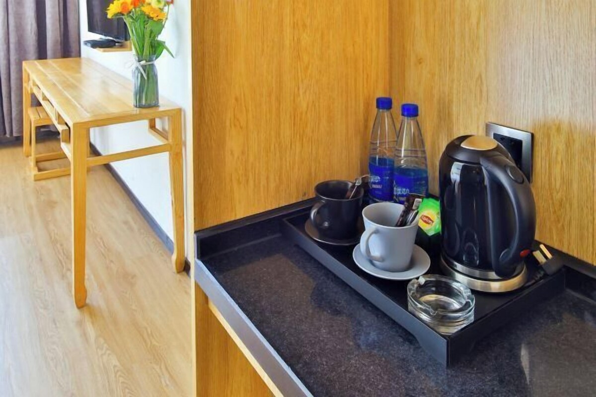Een hotelkamer met een houten tafel, een dienblad met een koffiezetapparaat, kopjes en een vaas met bloemen.