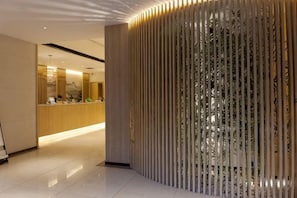 Un espace d’accueil doté d’un comptoir de réception en bois, d’un paravent vertical en bambou et d’un aménagement intérieur moderne.