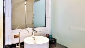 Een moderne badkamer met een rond wit wastafel, een grote spiegel en een douchecabine van glas.