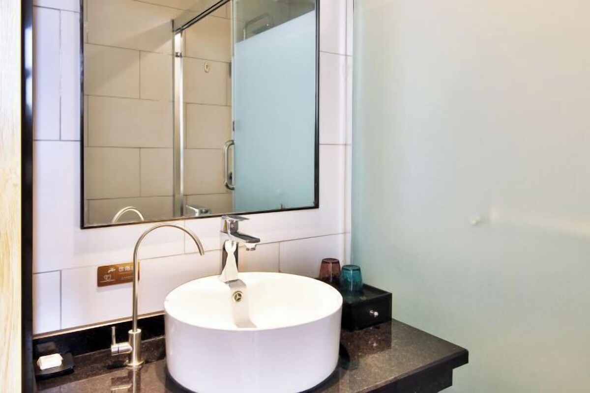 Een moderne badkamer met een rond wit wastafel, een grote spiegel en een douchecabine van glas.
