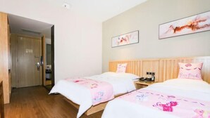 Een hotelkamer met twee bedden, elk met een roze deken met tekenfilmfiguren. Twee ingelijste foto’s aan de muur, een houten deur en een houten vloer.