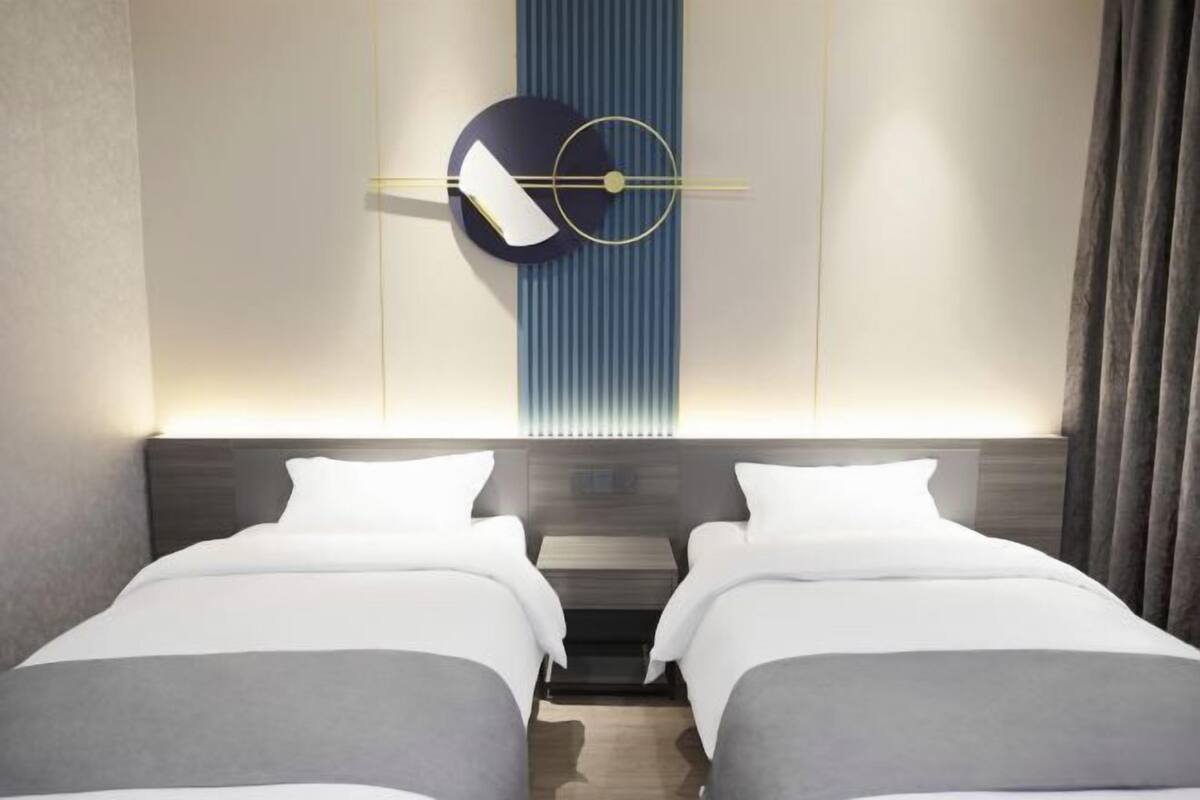 Une chambre d’hôtel avec deux lits, une horloge murale moderne et un panneau lumineux vertical.