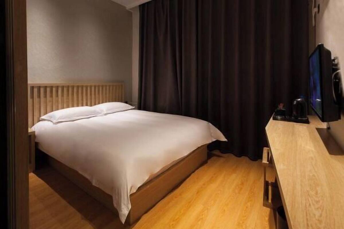 Une chambre d’hôtel avec un lit, un plancher en bois, un bureau avec une télévision et une fenêtre avec des rideaux.
