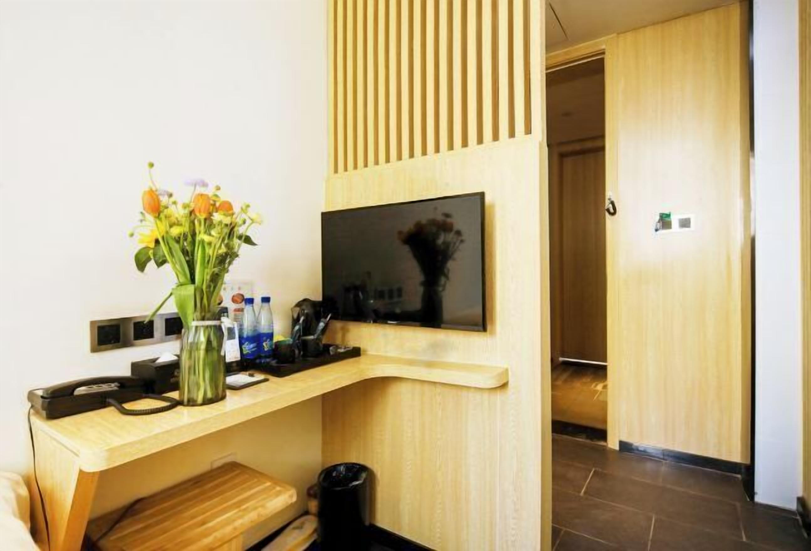 Ett modernt hotellrum med ett skrivbord i trä, en platt-TV, en vas med blommor och en papperskorg.