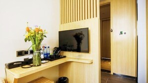 Een moderne hotelkamer met een houten bureau, een flatscreen televisie, een vaas met bloemen en een prullenbak.
