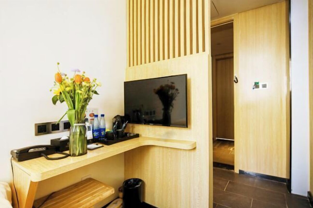 Een moderne hotelkamer met een houten bureau, een flatscreen televisie, een vaas met bloemen en een prullenbak.