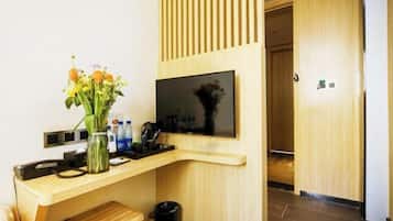 A modern hotel room with a wooden desk, a flat-screen TV, a vase with flowers, and a trash bin.