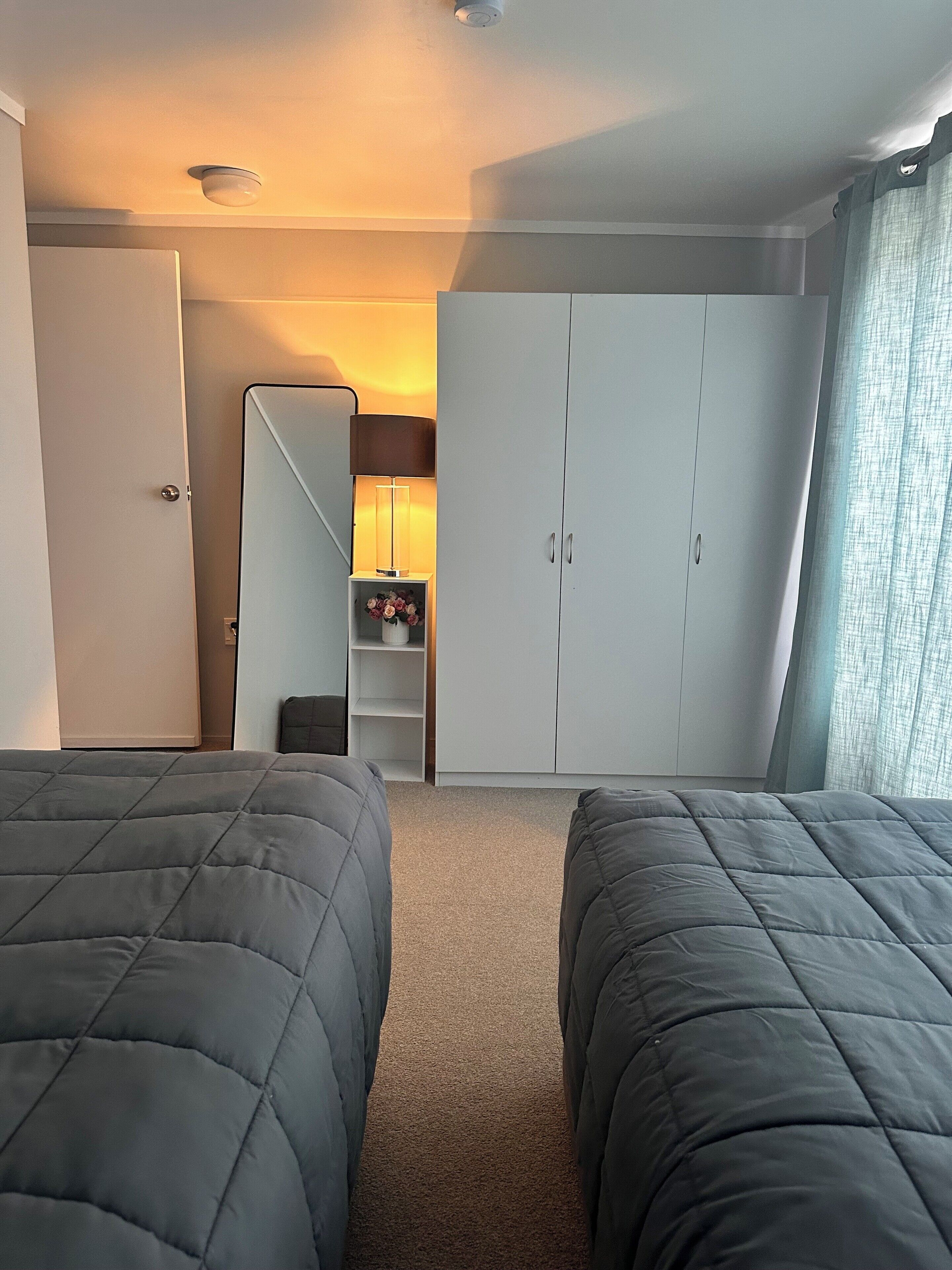 Ein Hotelzimmer mit zwei Betten, einem Kleiderschrank, einem Spiegel und einem kleinen Tisch mit Blumen.