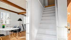 Un intérieur moderne avec un escalier blanc, un coin repas comprenant une table et des chaises, et une fenêtre donnant sur la verdure.