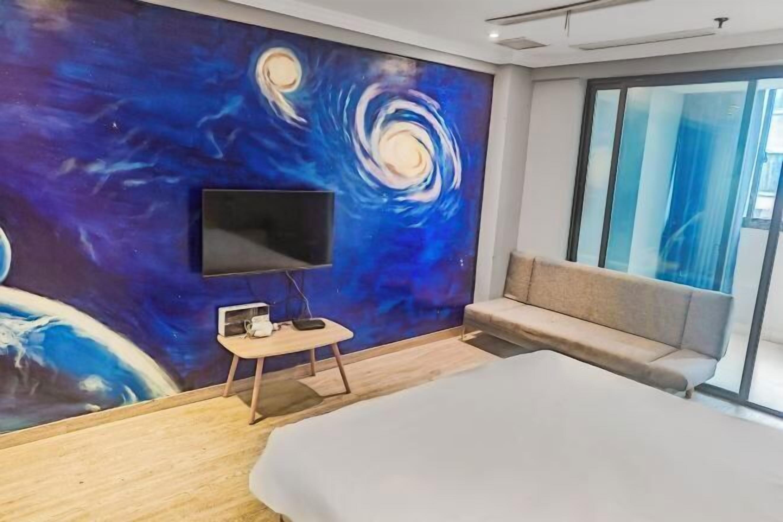 Una habitación de hotel moderna con una cama grande, un televisor de pantalla plana en la pared, una mesita auxiliar pequeña y un sofá.