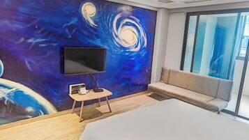 Una habitación de hotel moderna con una cama grande, un televisor de pantalla plana en la pared, una mesita auxiliar pequeña y un sofá.
