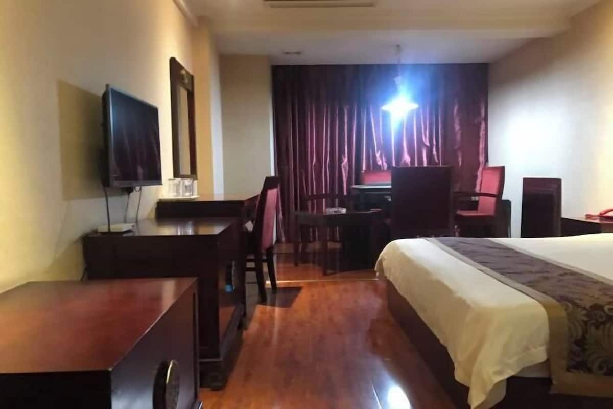 Une chambre d’hôtel avec un lit, un bureau, une chaise, une télévision et un rideau.
