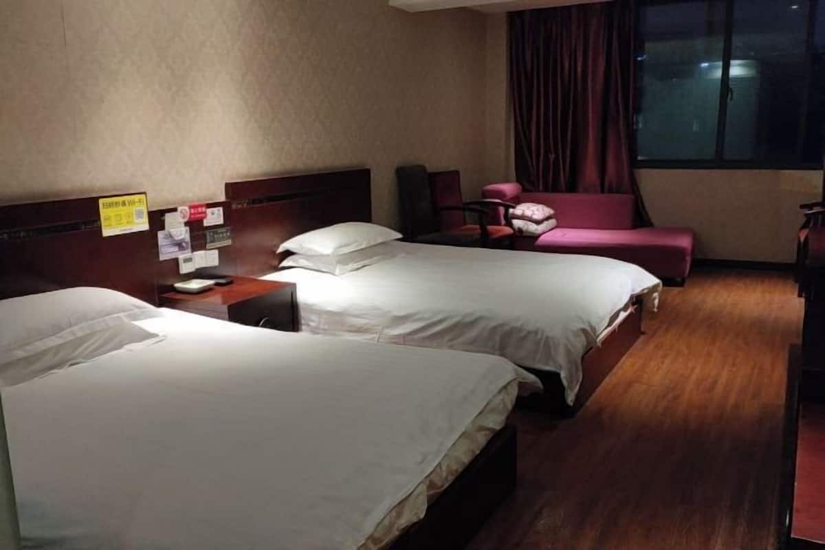 Une chambre d’hôtel avec deux lits, un bureau avec une chaise et une fenêtre avec des rideaux.