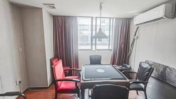 A room with a dining table, chairs, a laptop, and a window with curtains.