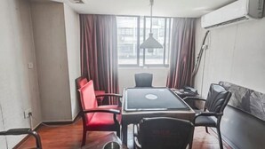 A room with a wooden floor, a table with a laptop, red and black chairs, a hanging lamp, and an air conditioning unit. - FanYing Business Hotel (Huzhou)