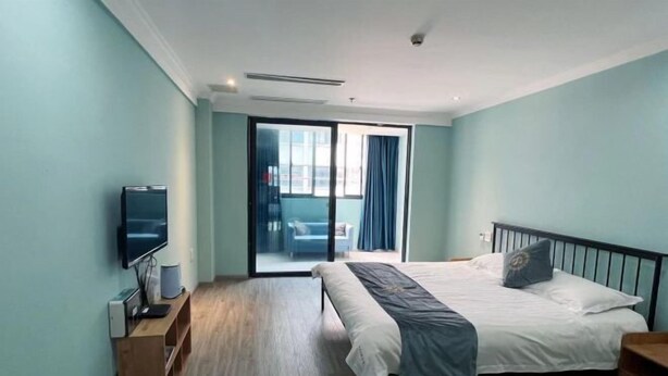 A modern hotel room with a bed, a TV, and a sliding door to a balcony. - FanYing Business Hotel (Huzhou)