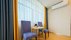 A room with two blue chairs, a small round table with a kettle, and a window with sheer curtains. - Anxin Intercity Hotel (Quanzhou Quangang) (Quanzhou)