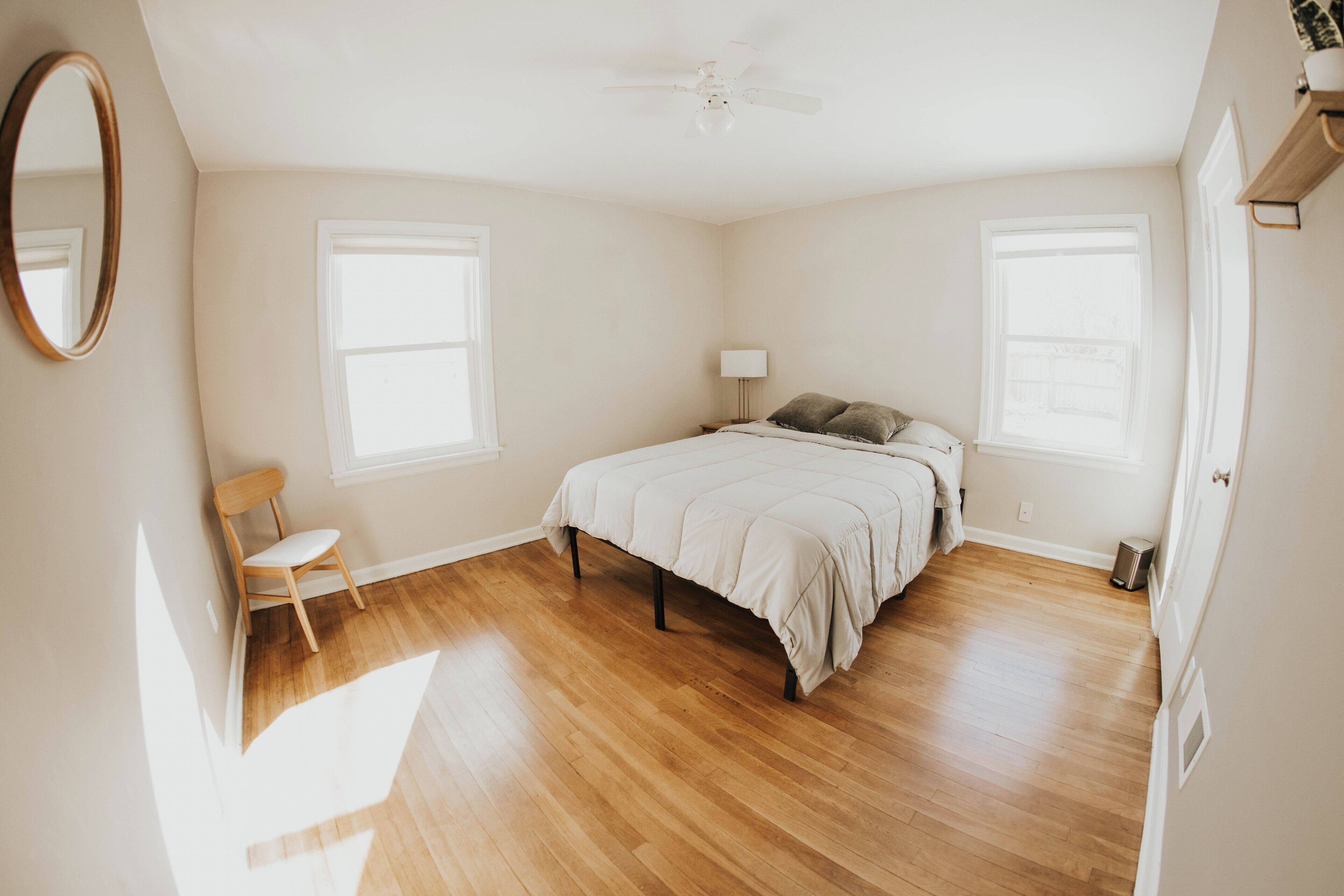 Un dormitorio con una cama, una silla, un ventilador de techo y dos ventanas.