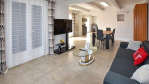 A modern living room with a glass coffee table, a dark sofa, and a dining area in the background. - Luxurious home in Sarrians (Sarrians)