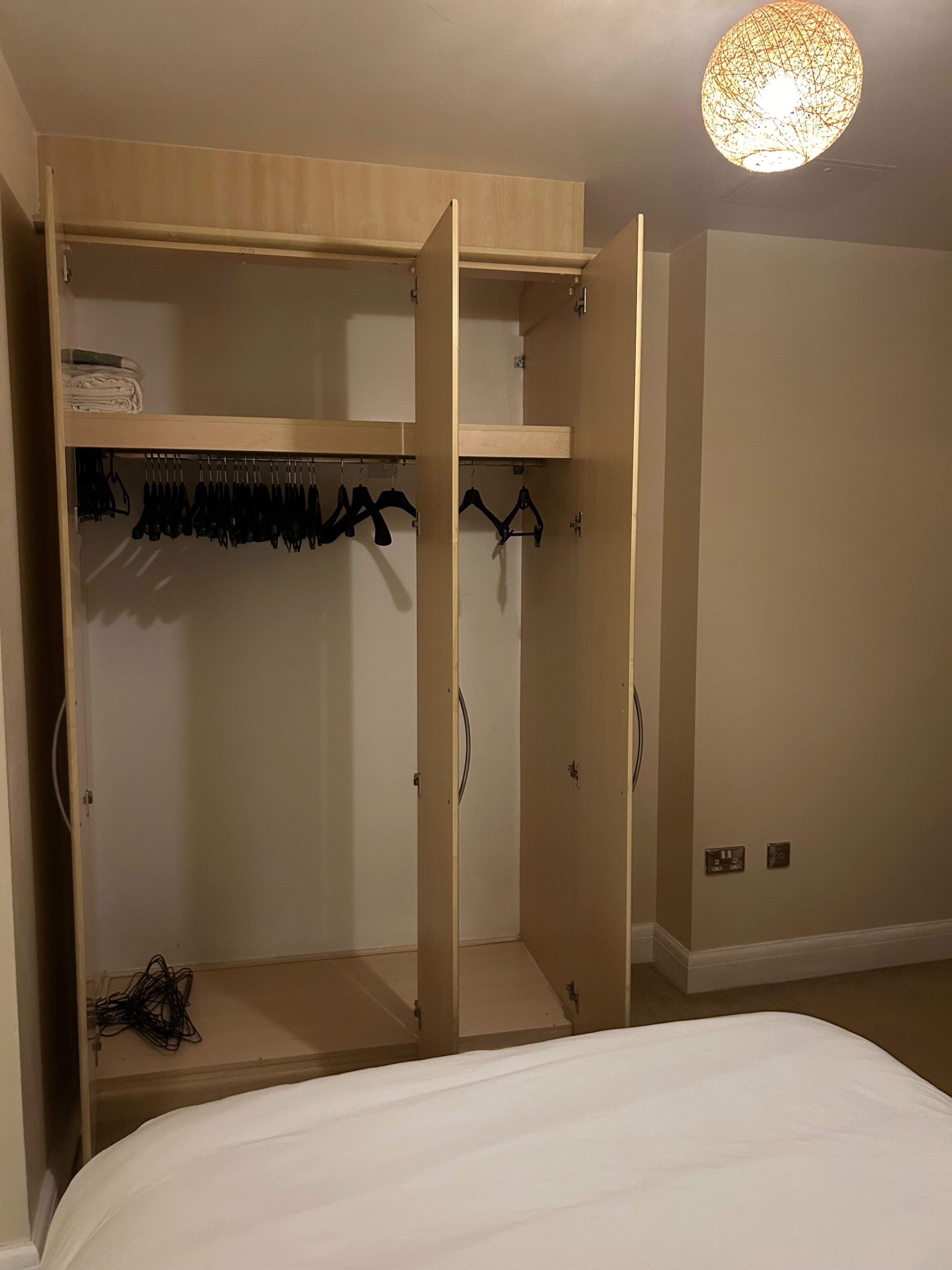 Une chambre avec un grand lit, une armoire en bois dont les portes sont ouvertes, et un porte-manteau mural.