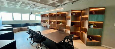 Uma sala de conferências moderna com uma mesa comprida, cadeiras de escritório pretas e estantes de madeira embutidas com plantas.