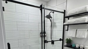 Un baño moderno con ducha de vidrio, azulejos blancos, un inodoro y un estante con toallas.