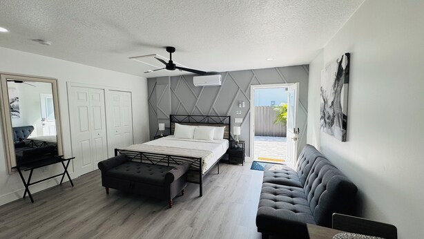 Un dormitorio moderno con cama, banqueta, ventilador de techo y vista al exterior.