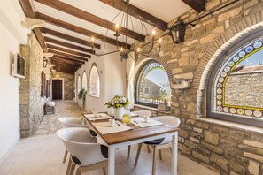 Enjoy a warm meal in this inviting dining area with a stone wall, wooden beams, and a beautiful view through the stained glass window.