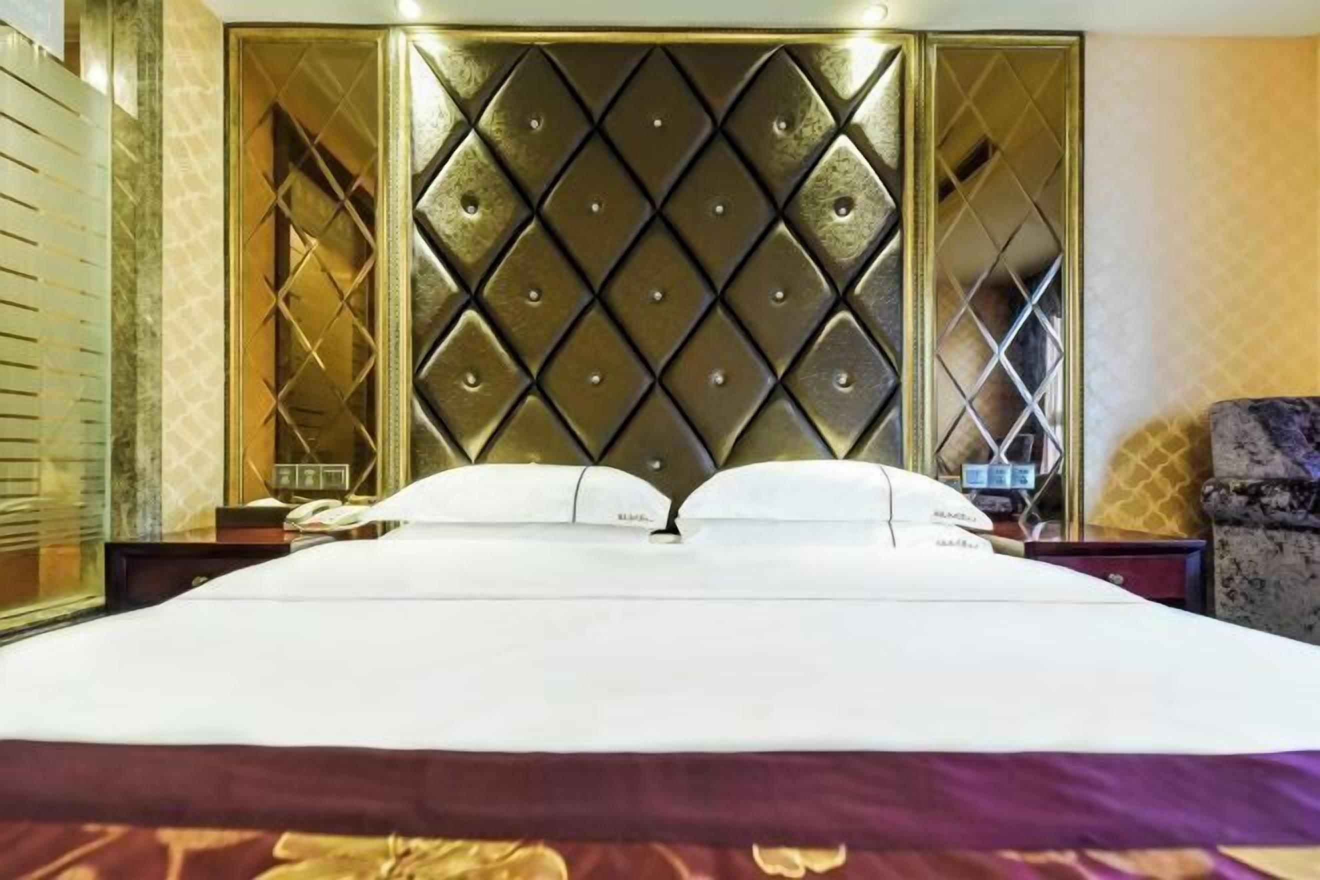 Ein Hotelzimmer mit einem großen Bett, einem Kopfteil mit Rautenmuster, einem Nachttisch mit Lampe und einem Sessel.