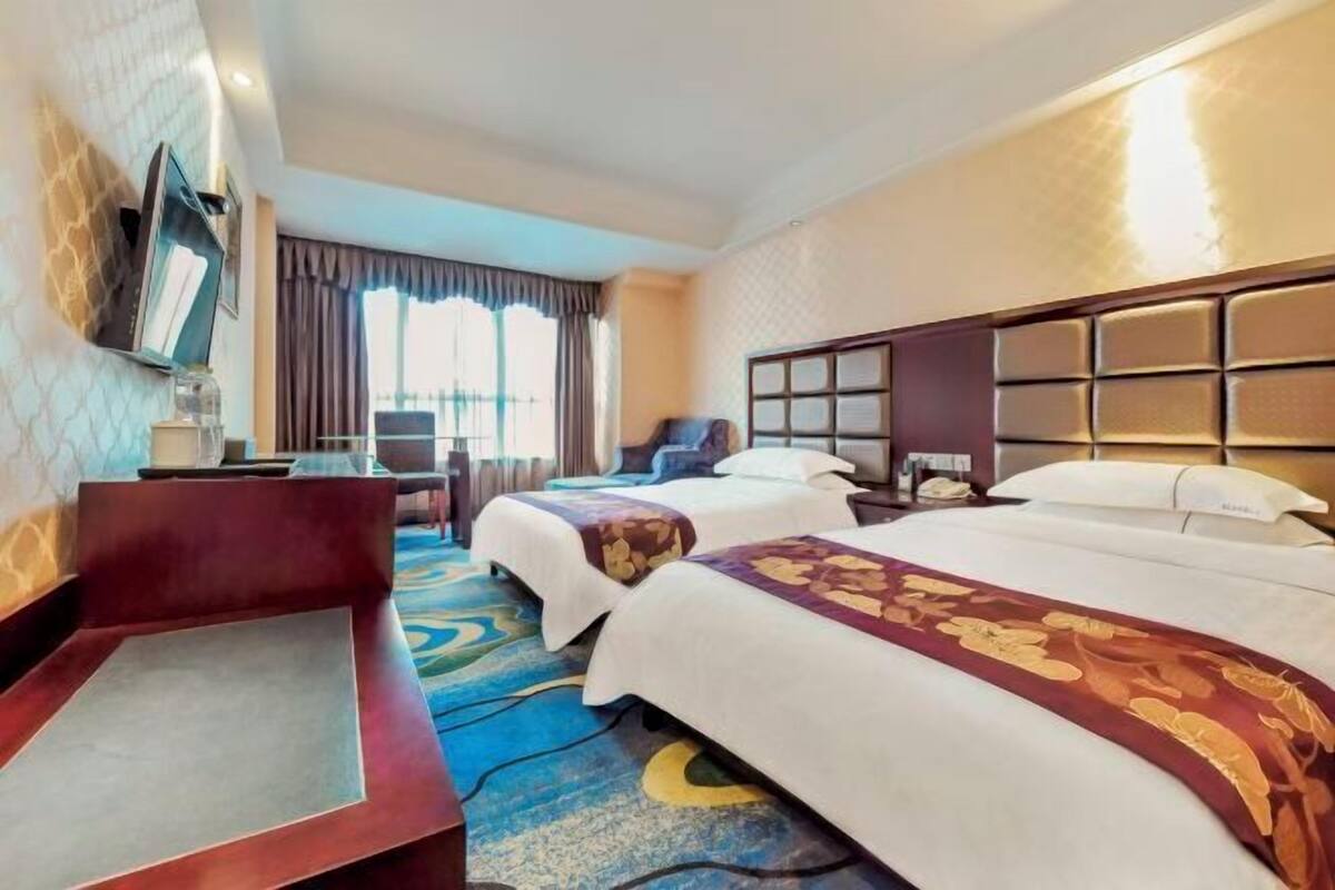 A hotel room with two beds, a TV, a desk, and a window with curtains.