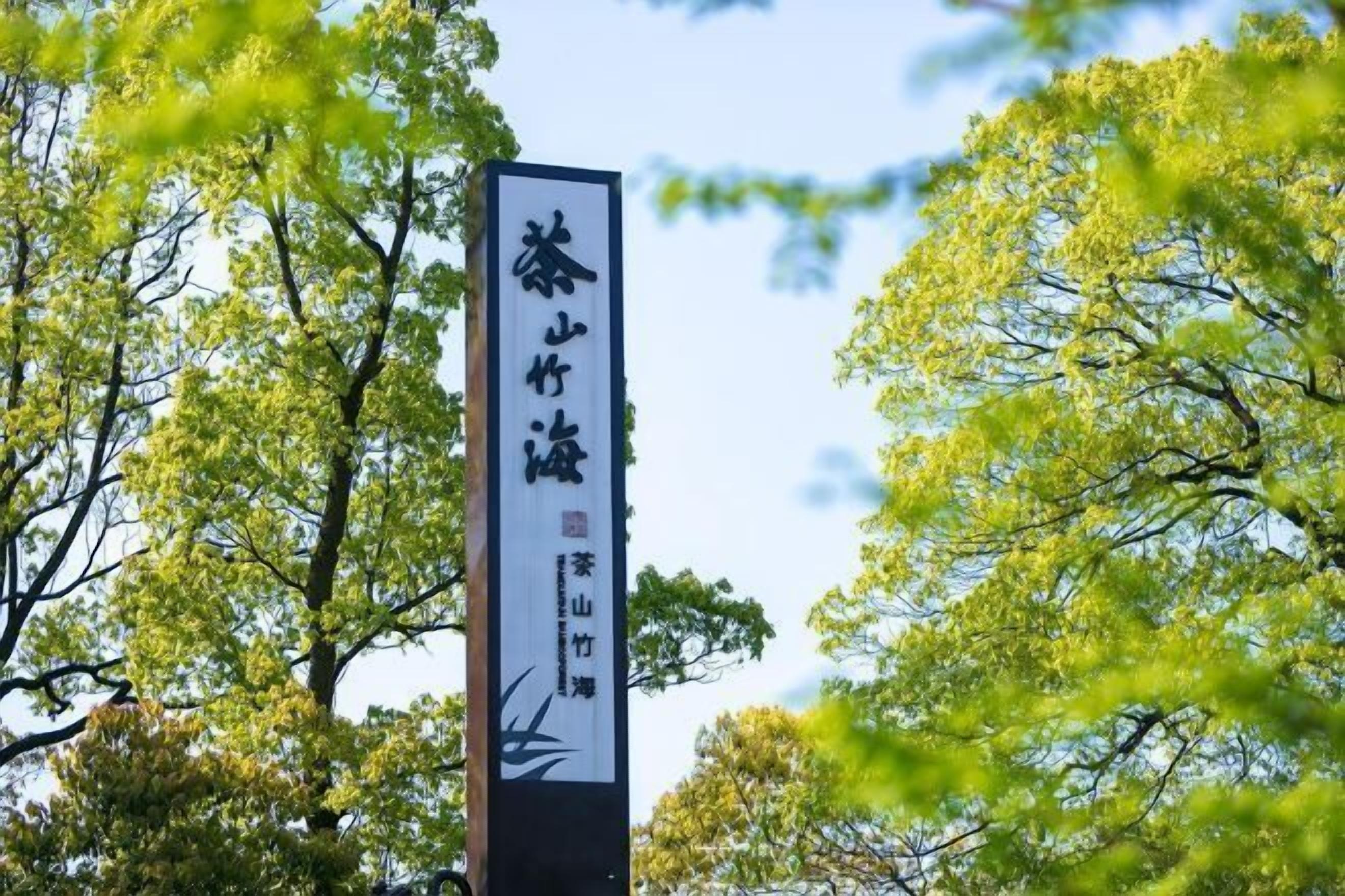 A vertical sign with Japanese characters, surrounded by trees.