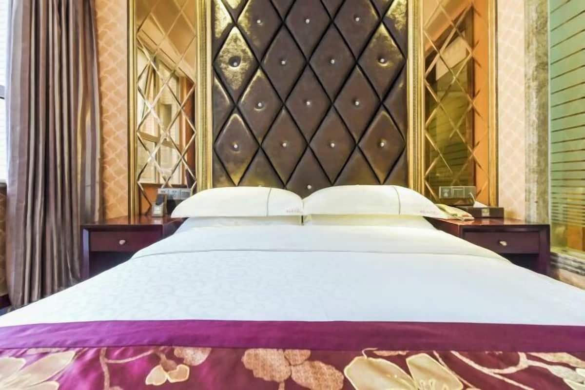 A hotel room with a large bed, a tufted headboard, a nightstand with a lamp, and a window with curtains.