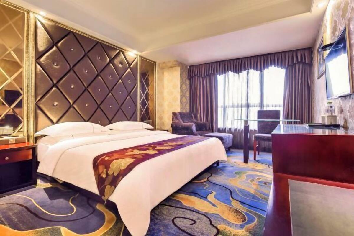 A hotel room with a large bed, a desk, a chair, and a window with curtains.
