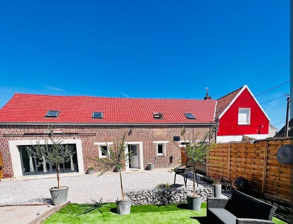 Ein rot genutztes Haus mit rotem Dach, einem kleinen Garten und einem Holzzaun.