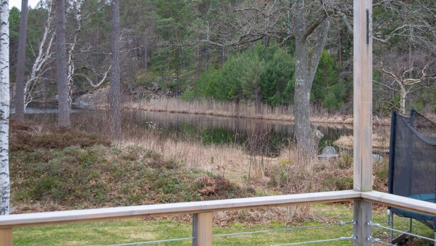 A view from a balcony overlooking a pond surrounded by trees, with a metal railing and a trampoline in the foreground. - Gorgeous home in Värmdö with sauna (Värmdö)