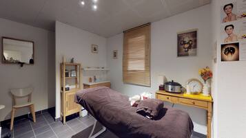 A room with a massage table, wooden cabinet, and a small desk with a clock and flowers.