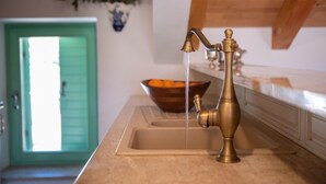 Una cocina con un grifo de latón, un cuenco de madera y una puerta verde.
