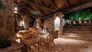 Un patio exterior de piedra con mobiliario de madera rústica, escalones de piedra y plantas en macetas.