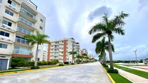 Un edificio residencial de varios pisos con balcones, una acera bien cuidada y palmeras.
