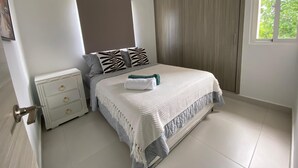 Un dormitorio con cama, mesita de noche, cómoda, equipo de aire acondicionado, ventana y puerta.