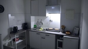 Une cuisine compacte avec des meubles blancs, un évier, une machine à café et un petit réfrigérateur.