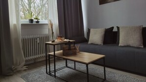 Un salon moderne avec un canapé de couleur foncée, une table basse en bois, un radiateur et une fenêtre avec des rideaux.