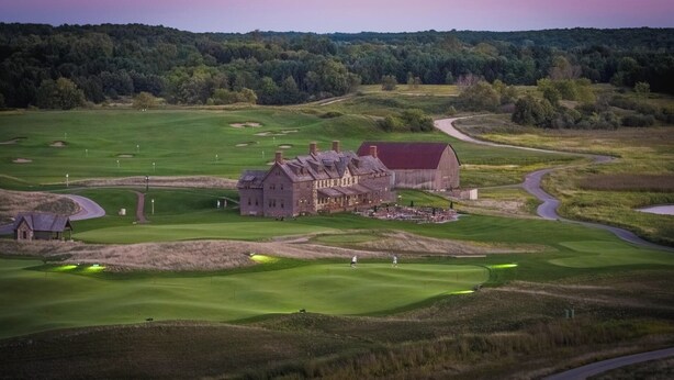 A large, historic building with multiple wings, surrounded by a well-maintained golf course.