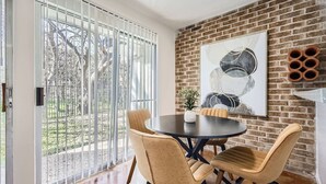 A dining area with a brick wall, a large abstract painting, and a view through a sliding glass door.
