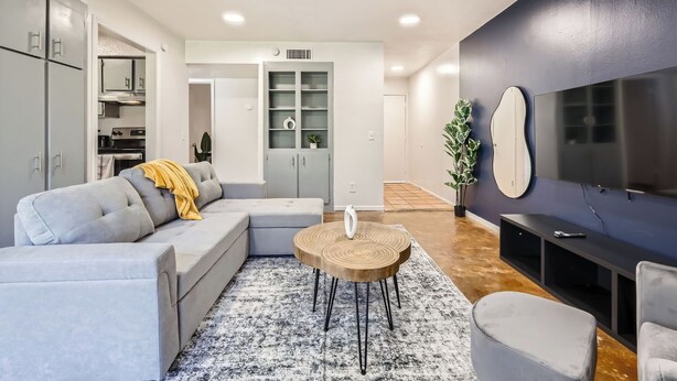 A modern living room with a grey sofa, a round wooden coffee table, a flat-screen TV, and a built-in cabinet.