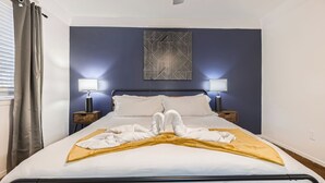 A neatly made bed with a white comforter and a yellow throw blanket, two bedside lamps, and a geometric wall art piece above the bed.