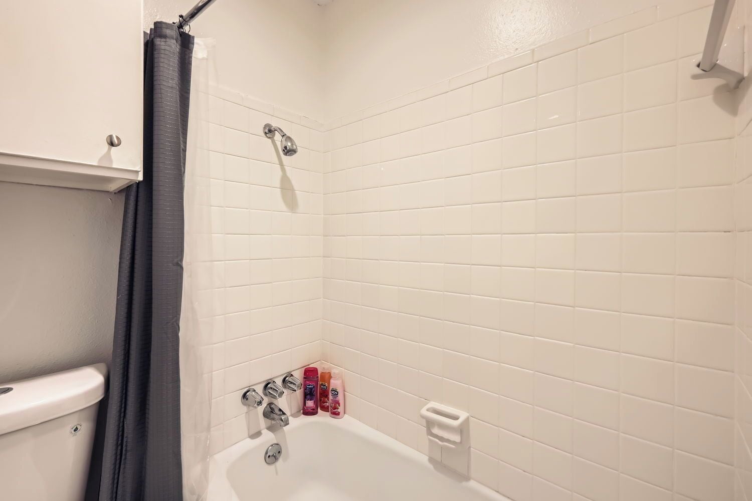 A bathroom with white tiled walls, a bathtub, a showerhead, and a toilet.